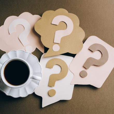 A cup of coffee on a table along with papercraft question marks