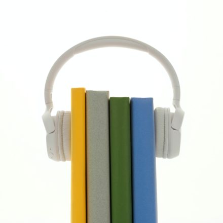 A pair of white wireless headphones is mounted on four books with different colored spines.