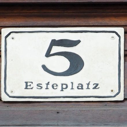 A black painted numeral 5 on a white plaque screwed to a wooden board