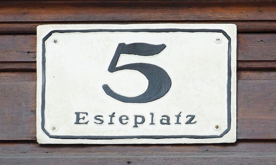 A black painted numeral 5 on a white plaque screwed to a wooden board