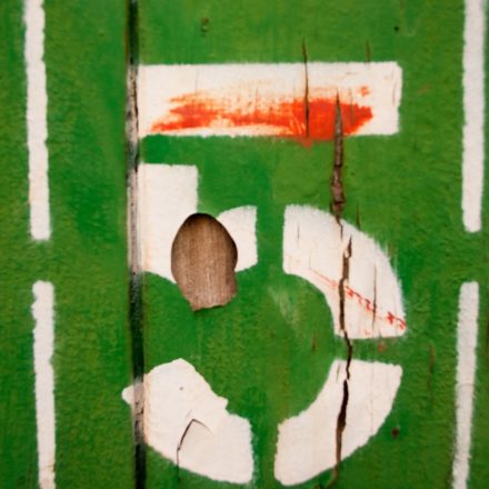 A stenciled white number five painted on a green wooden board