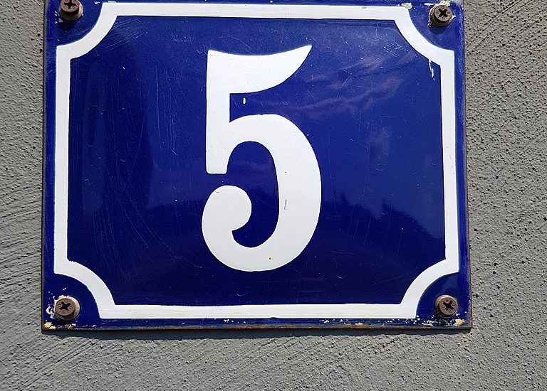 A white numeral 5 on a blue painted metal sign that has been screwed to a wall