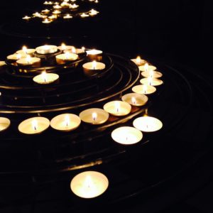 A color photo of several small candles lit in a darkened room