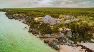 A color aerial photograph of Tulum, Mexico showing a sea, a beach, and ancient Mayan ruins atop rocky cliffs.