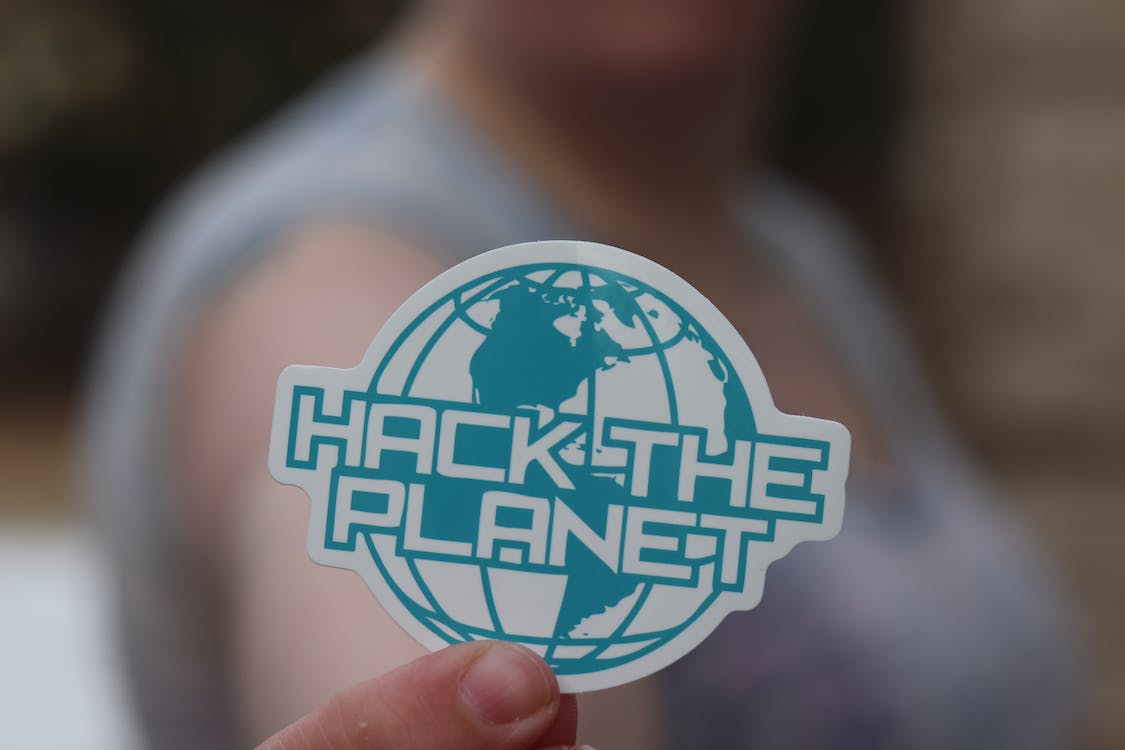 A person holding up a sticker that read "Hack the Planet"